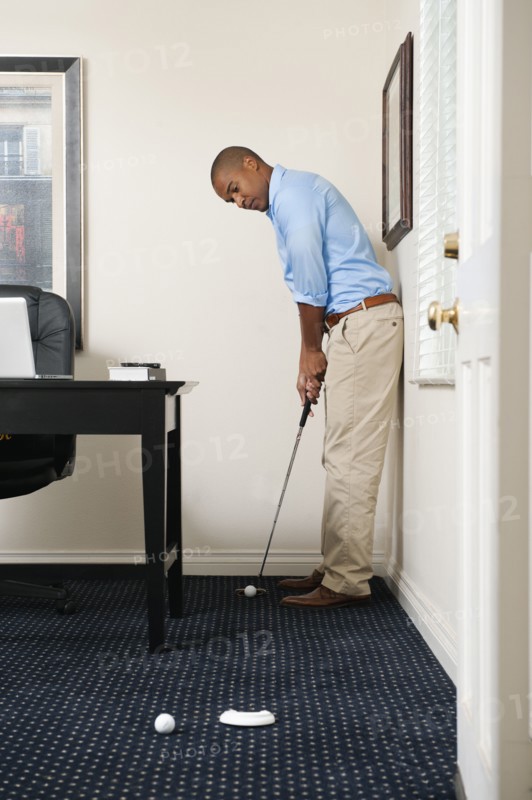 African American businessman putting golf ball