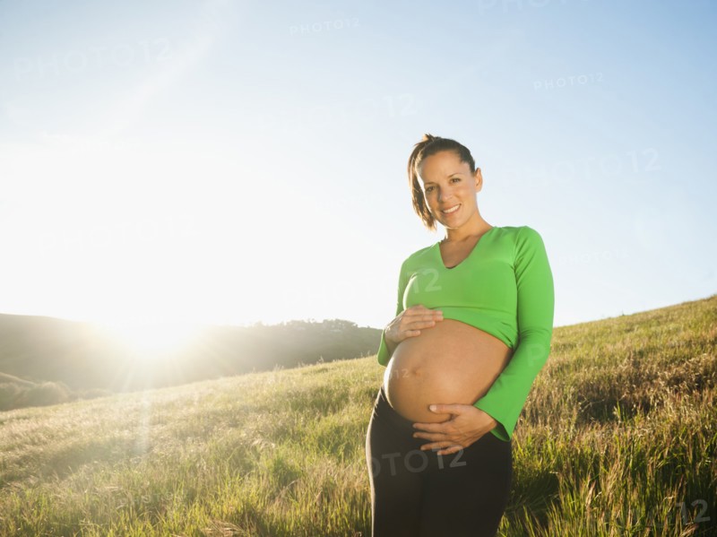 Pregnant Hispanic woman caressing stomach in field