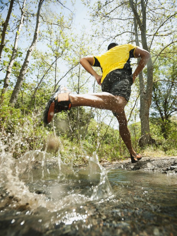 Mixed race man running through stream