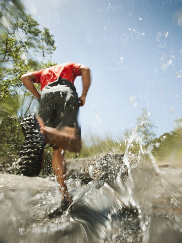 Mixed race man running through stream