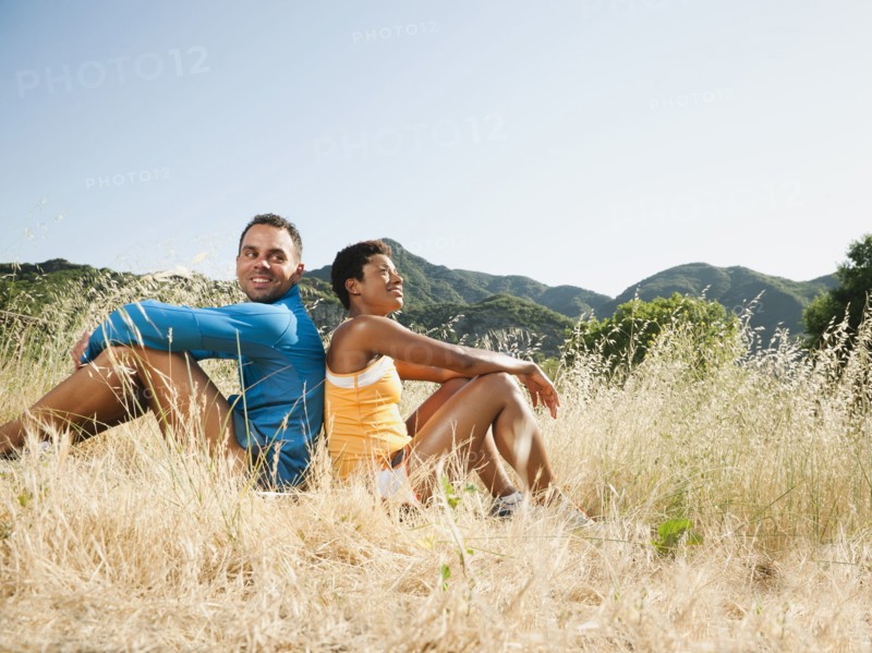 Couple sitting back to back in field after exercise