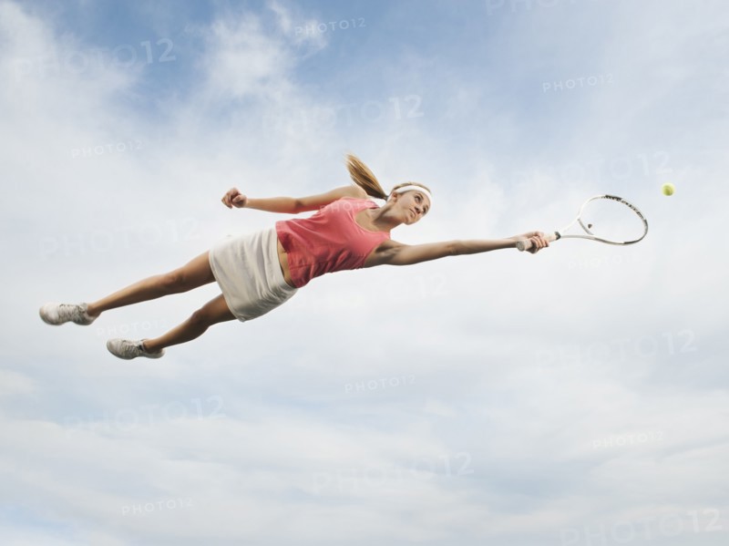 Caucasian woman jumping in mid-air playing tennis