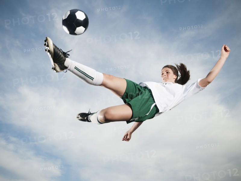 Caucasian teenager kicking soccer ball in mid-air