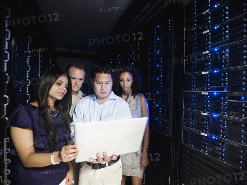 Business people looking at laptop in server room