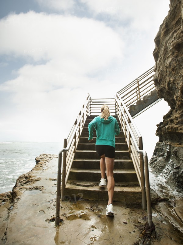 Caucasian woman running up stairs next to ocean