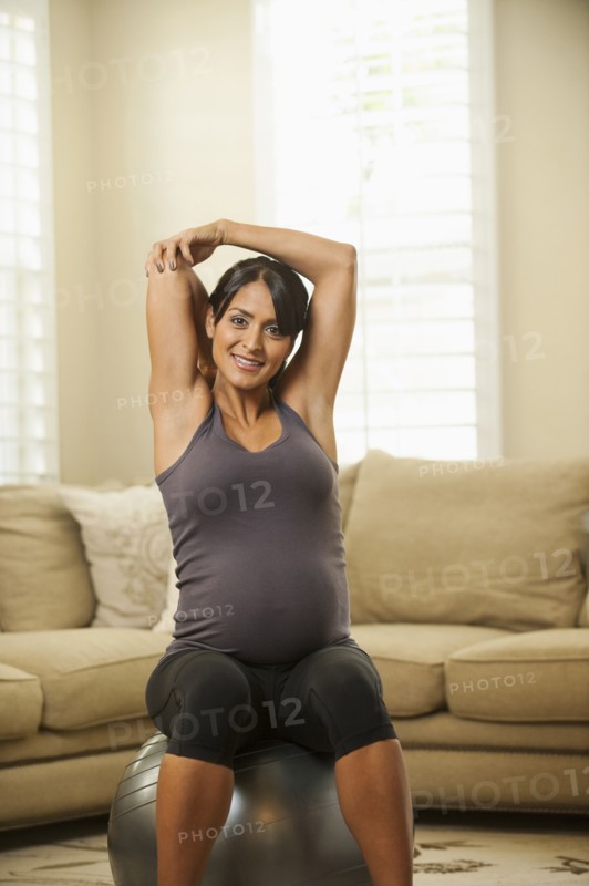 Pregnant Hispanic woman stretching on exercise ball
