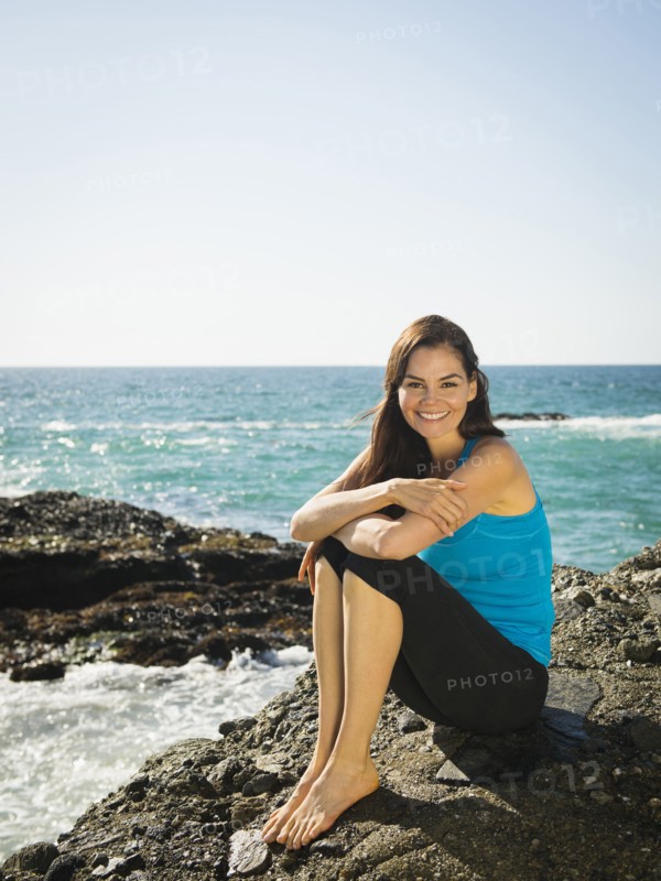 Mixed race woman smiling on rocky beach