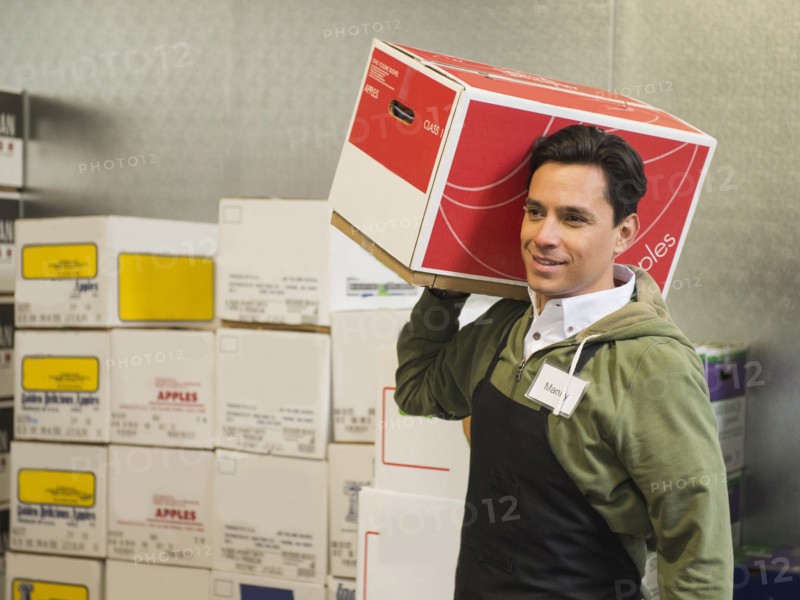 Hispanic worker carrying box in walk-in freezer
