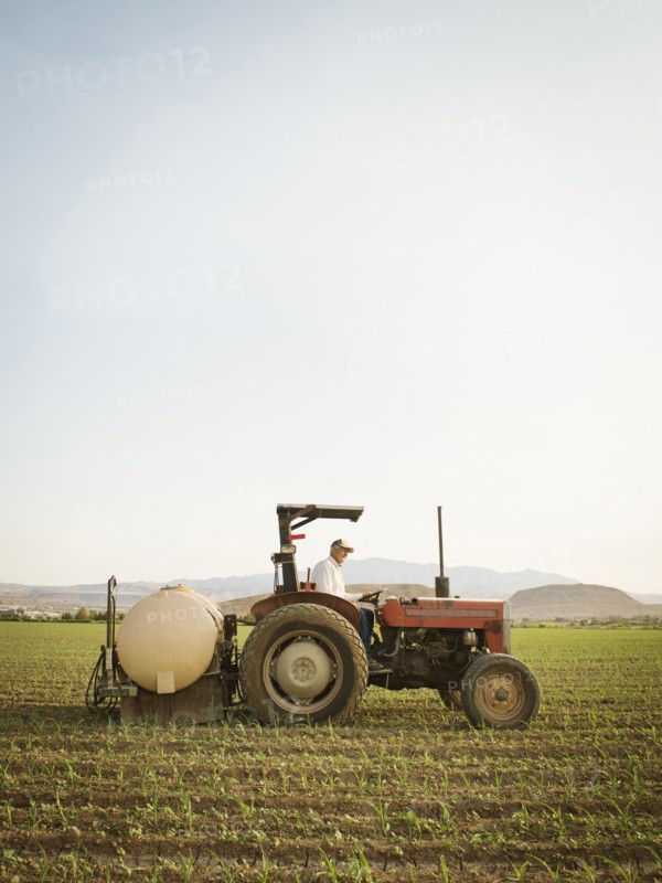 Caucasian farmer driving tractor in crop field