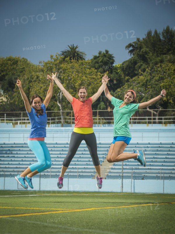 Caucasian women jumping for joy in stadium field