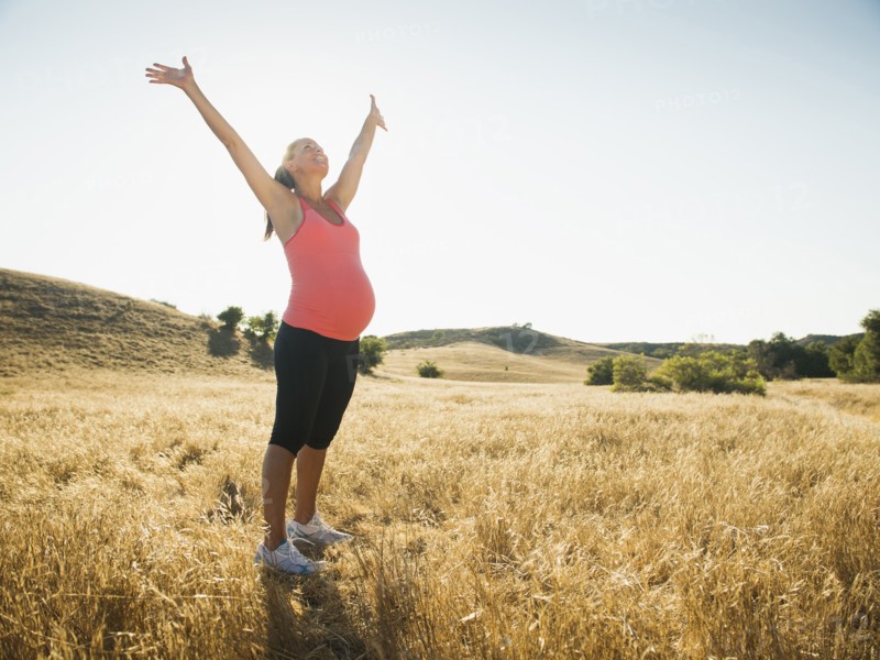 Pregnant Hispanic woman cheering in rural landscape