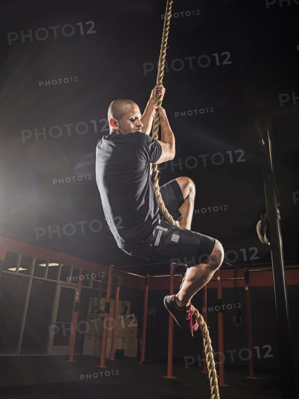 Hispanic man climbing rope in gym