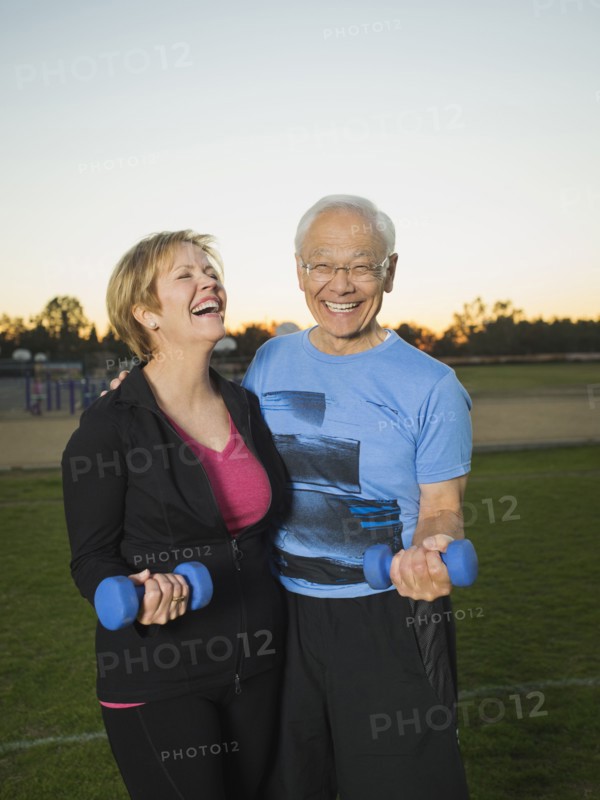 Older couple lifting weights together in urban park