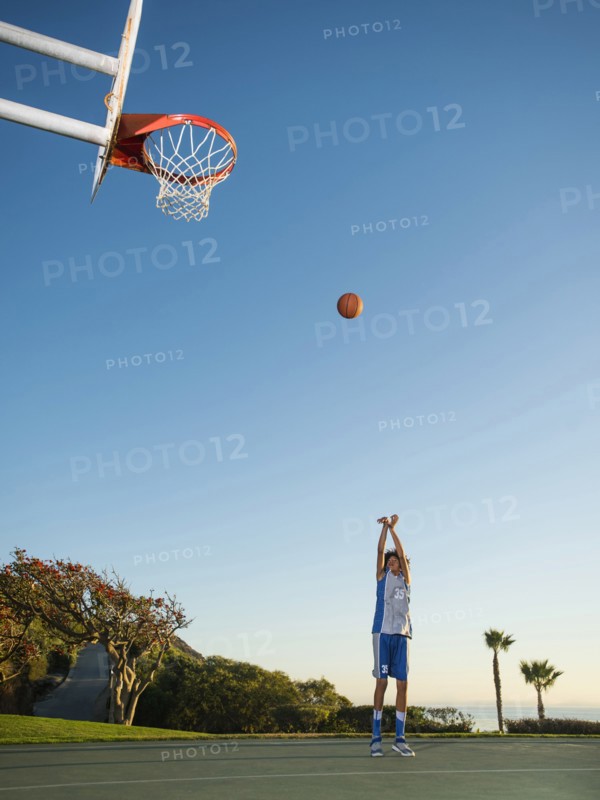 Black teenage boy shooting basketball on court