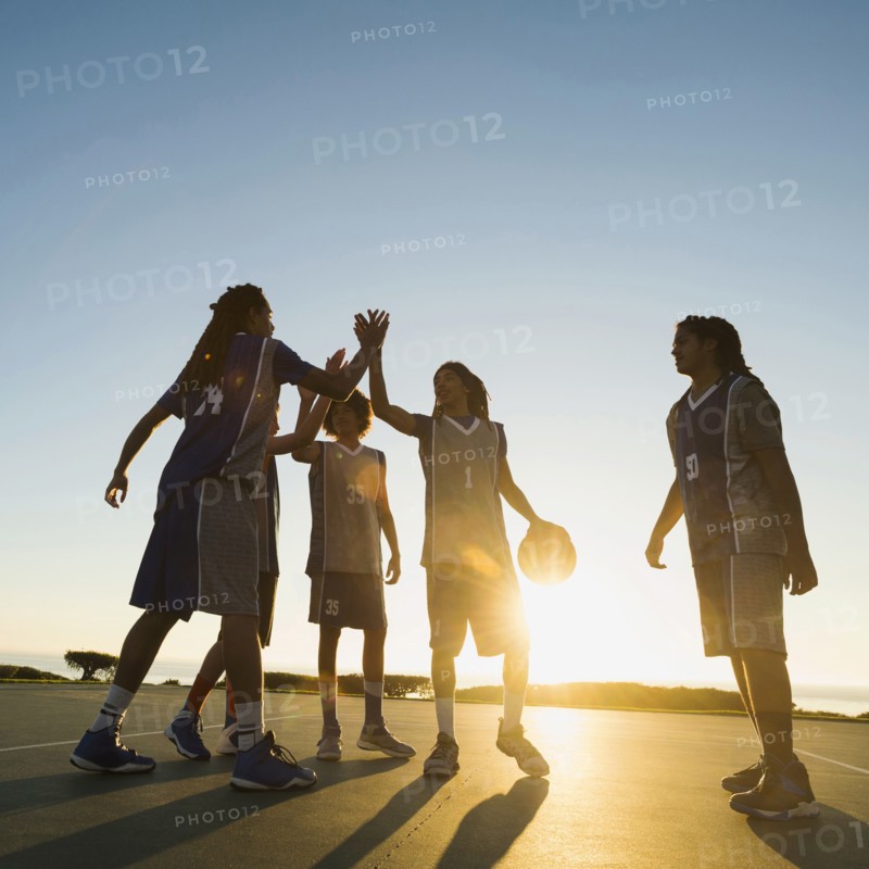 Back lit basketball team high fiving on court