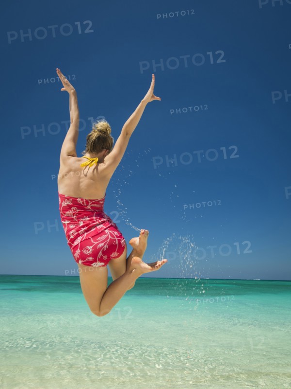 Caucasian woman jumping for joy in tropical ocean