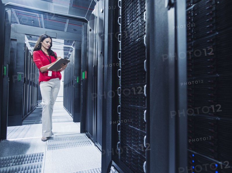Caucasian businesswoman reading clipboard in server room