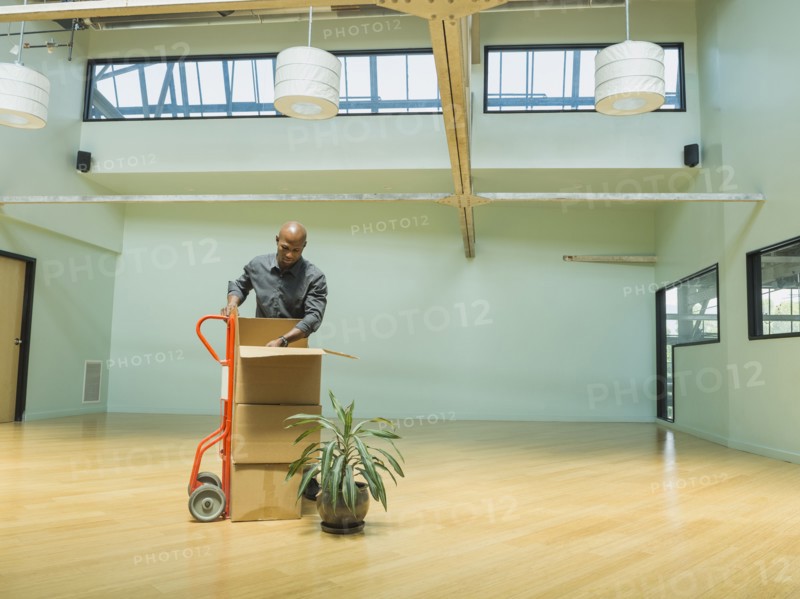 Black businessman unpacking cardboard boxes in empty office