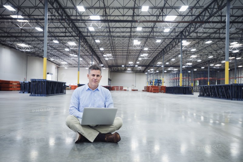 Caucasian businessman using laptop in empty warehouse
