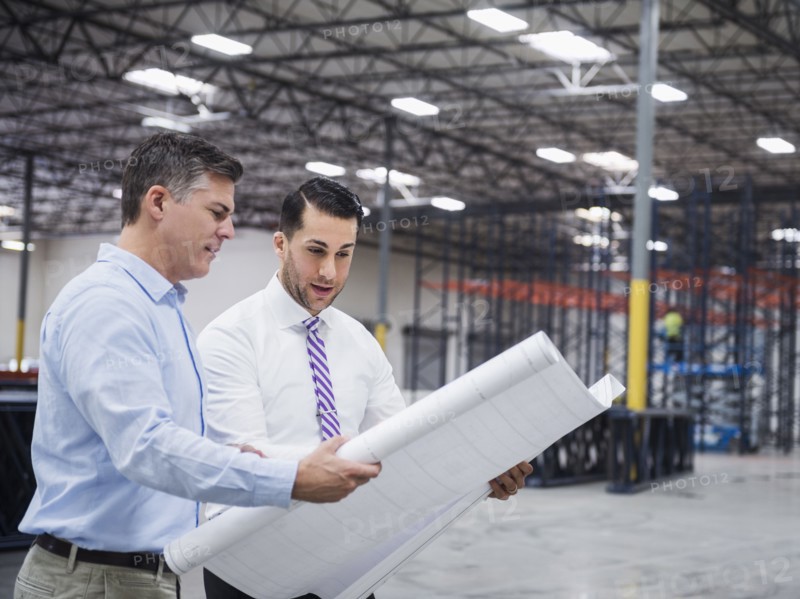 Caucasian architects reading blueprints in warehouse