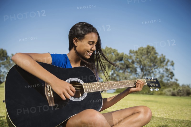 Mixed race girl playing guitar in park