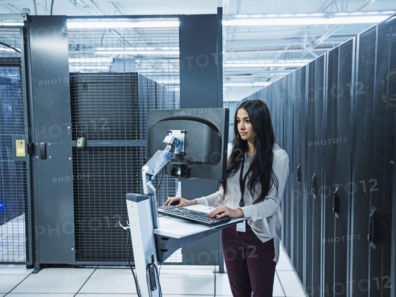 Mixed race technician using computer in server room