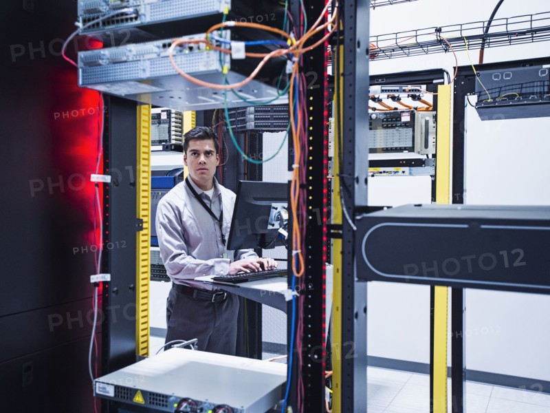 Hispanic technician using computer in server room