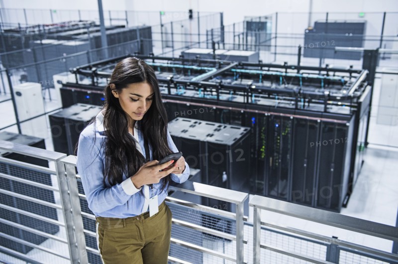 Mixed race businesswoman using cell phone on balcony over server room