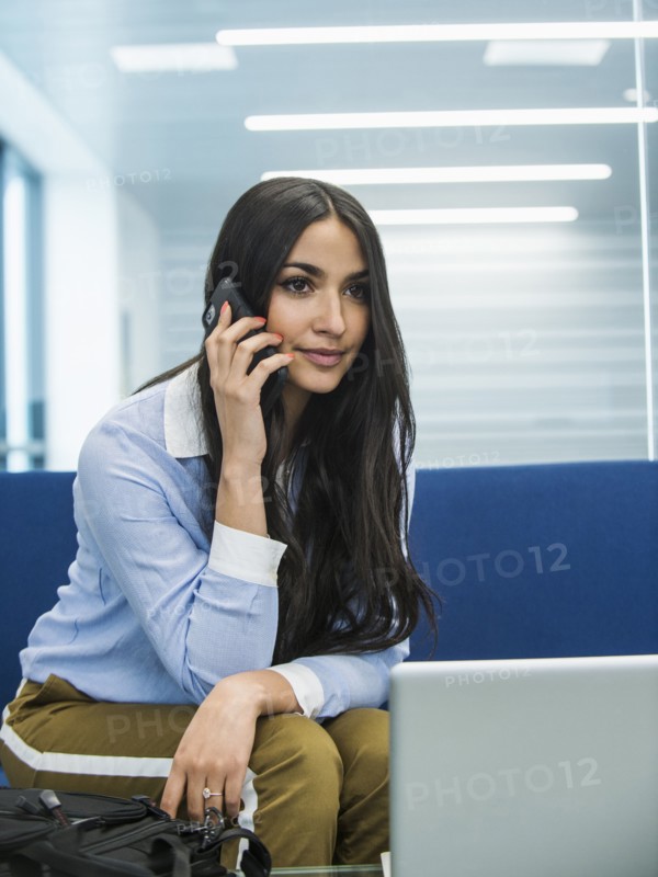 Mixed race businesswoman talking on cell phone in office lobby