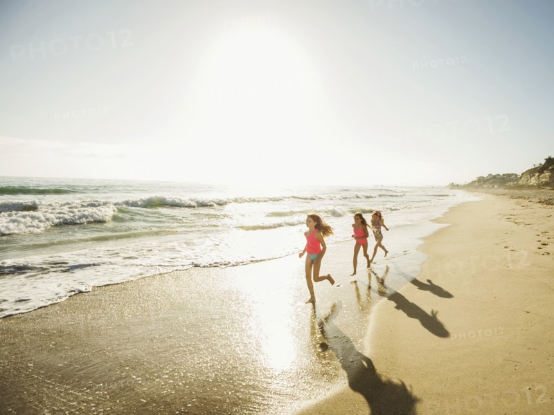 Caucasian sisters running on beach