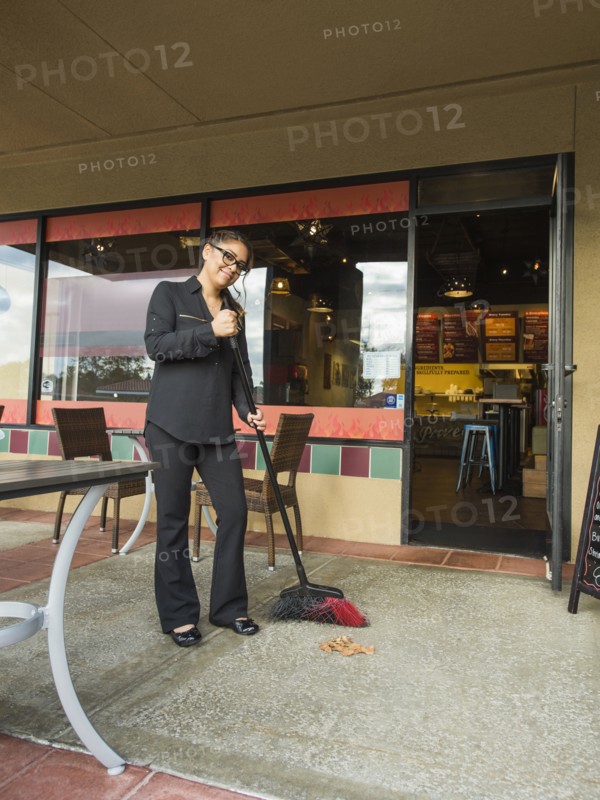 Hispanic business owner sweeping sidewalk