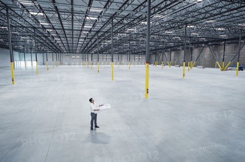 Indian architect holding blueprint in empty warehouse