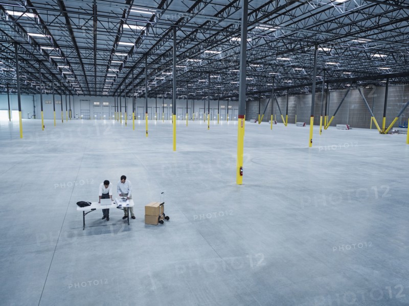 Architects using laptop and blueprint in empty warehouse
