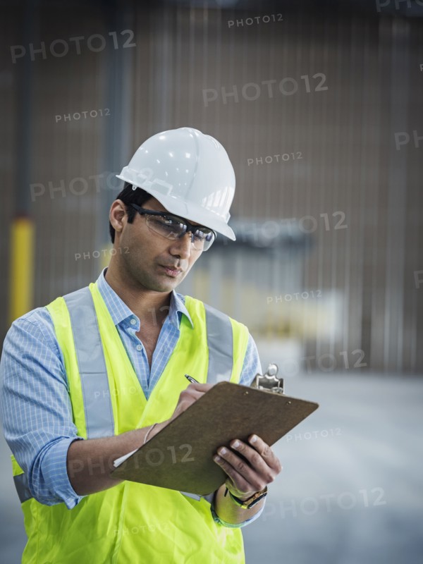 Smiling Indian worker writing on clipboard in empty warehouse