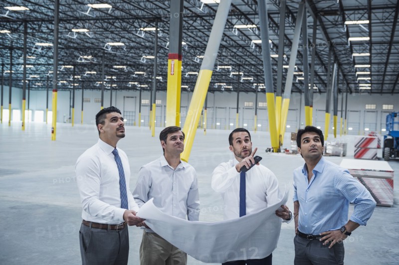 Architects examining blueprint in empty warehouse