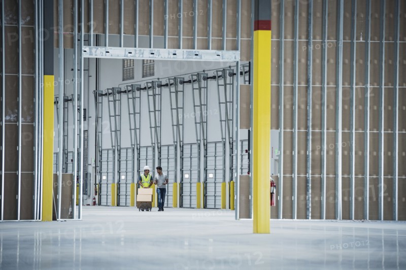 Workers with boxes on hand truck in empty warehouse