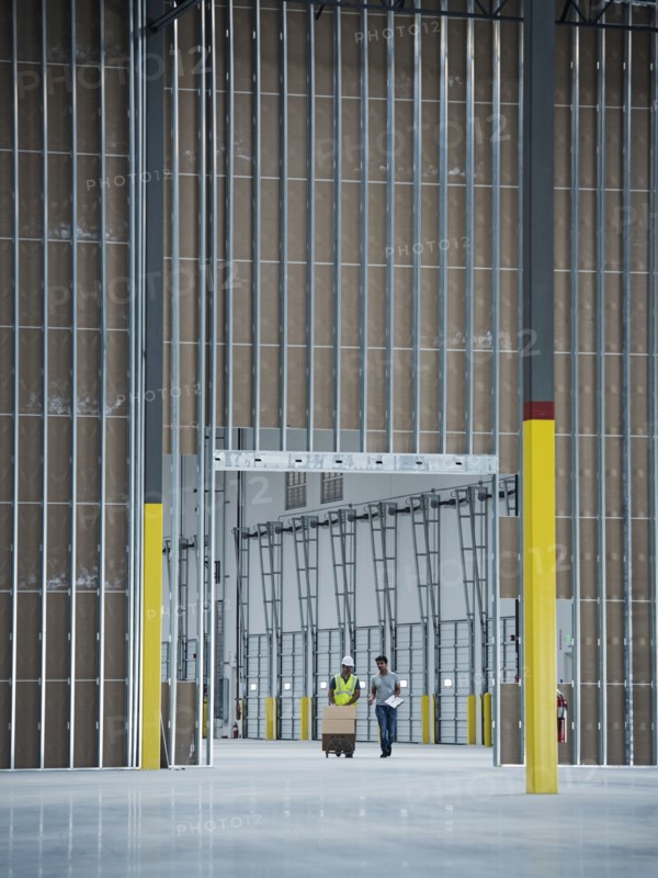 Workers with boxes on hand truck in empty warehouse
