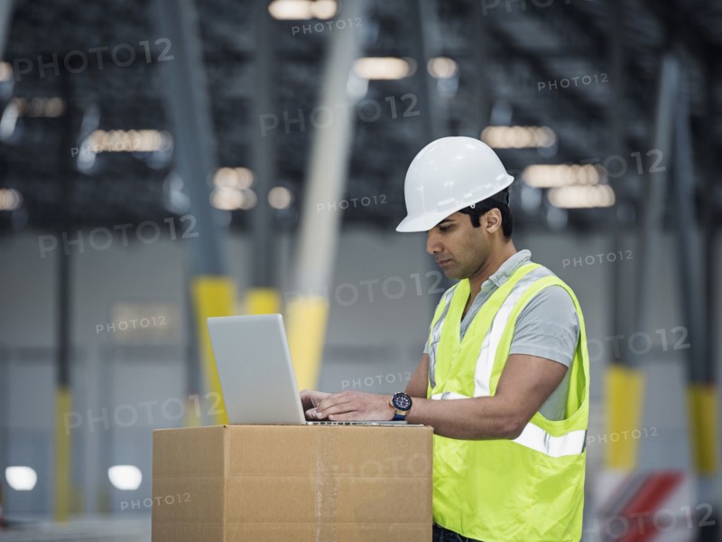 Indian worker using laptop on cardboard box in warehouse