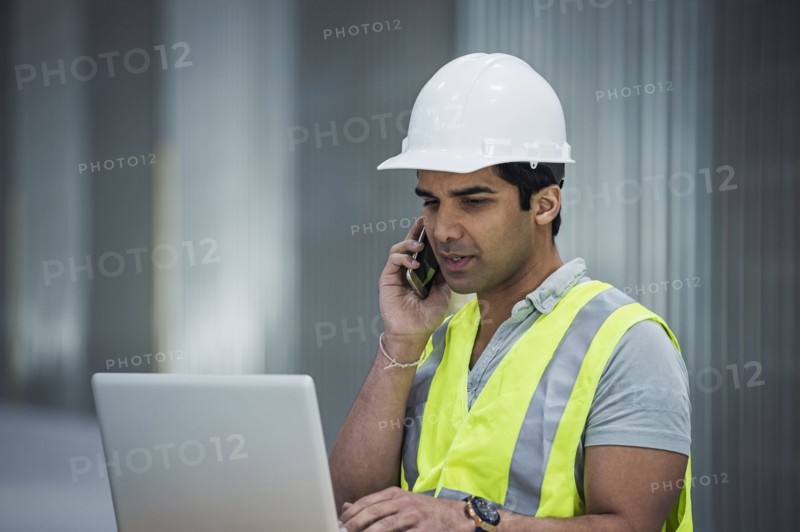 Indian worker using laptop and cell phone in warehouse