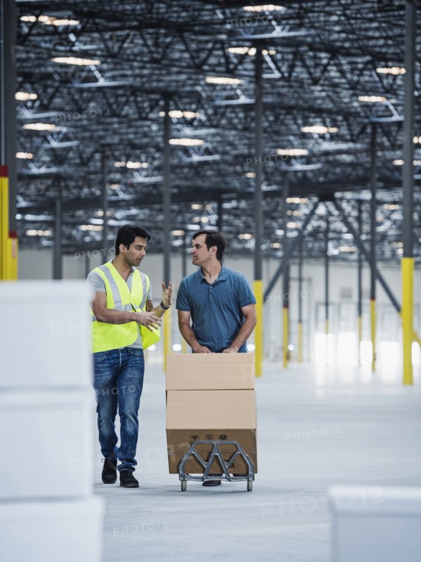 Workers pushing cardboard boxes on hand truck in warehouse