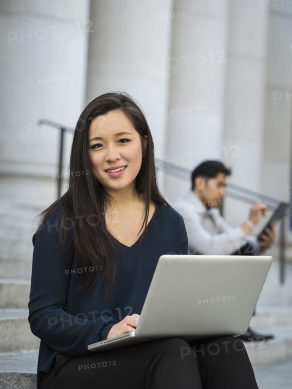Chinese businesswoman sitting on staircase using laptop