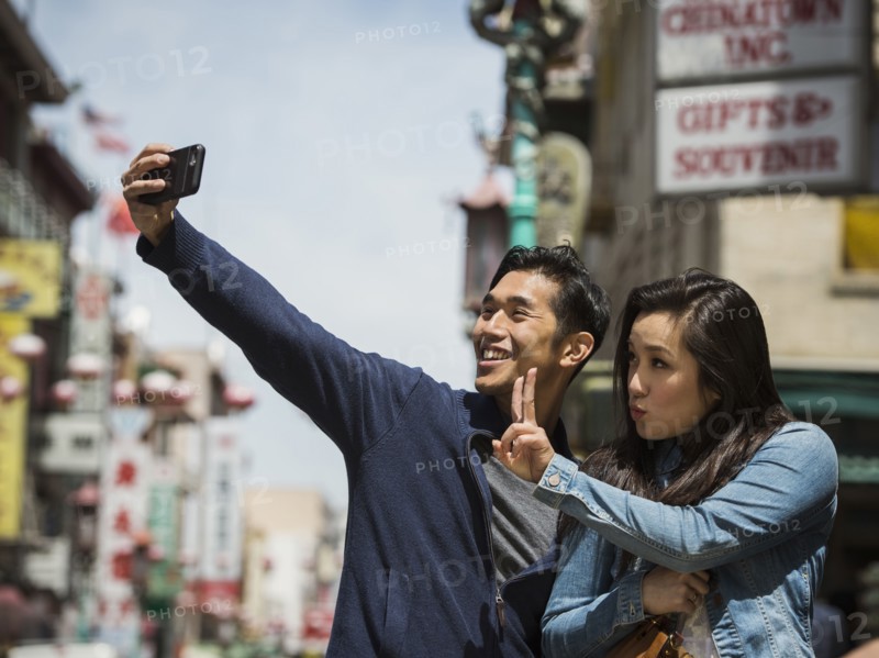 Smiling Chinese couple posing for cell phone selfie in city
