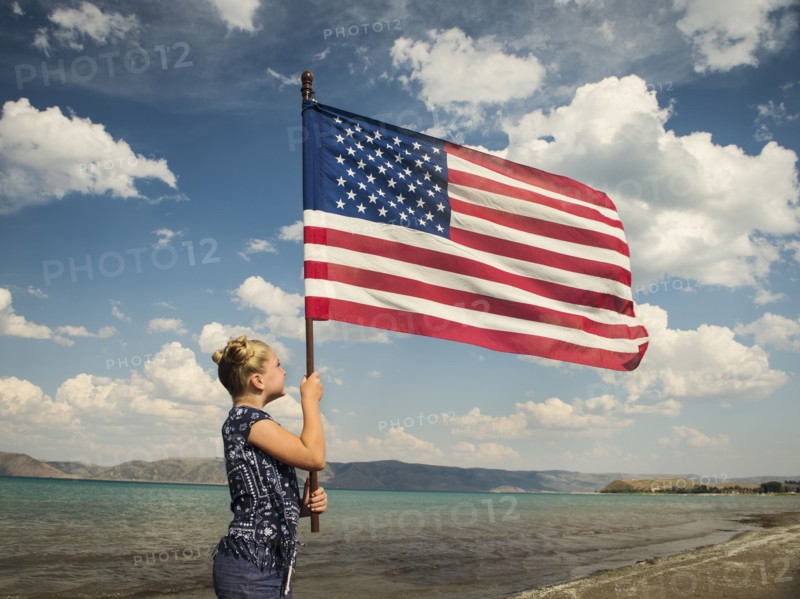Caucasian girl holding American flag at beach