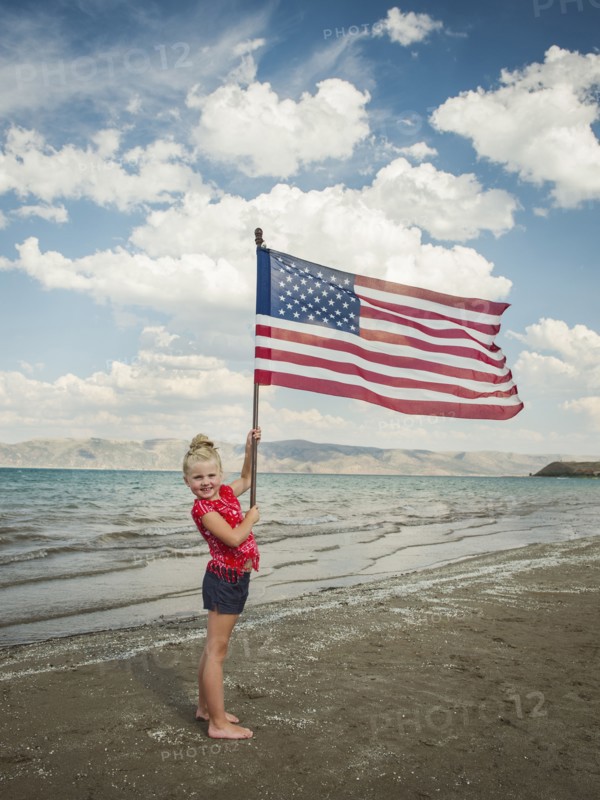 Caucasian girl holding American flag at beach