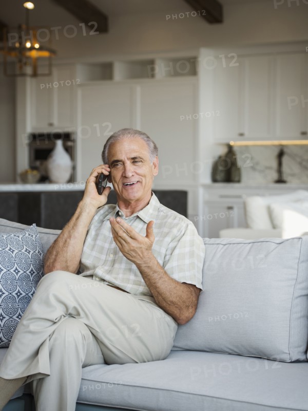 Caucasian man sitting on sofa talking on cell phone