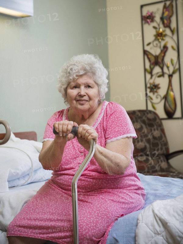 Smiling Caucasian woman sitting on bed leaning on cane