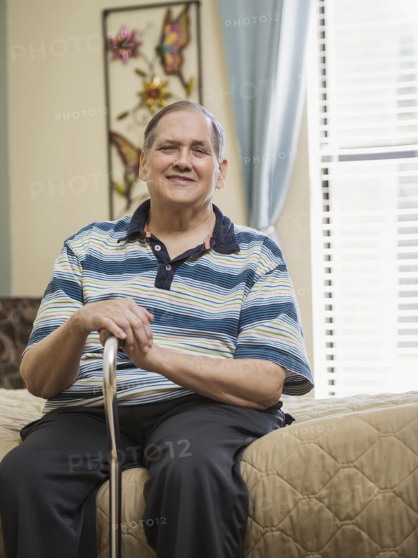 Smiling Caucasian man sitting on bed holding cane