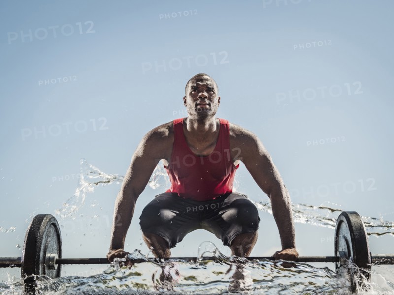 Water spraying on black man preparing for lifting barbell