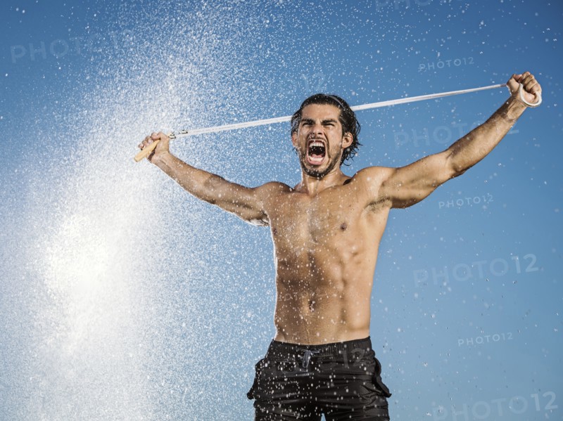 Water spraying on Hispanic man holding jump rope