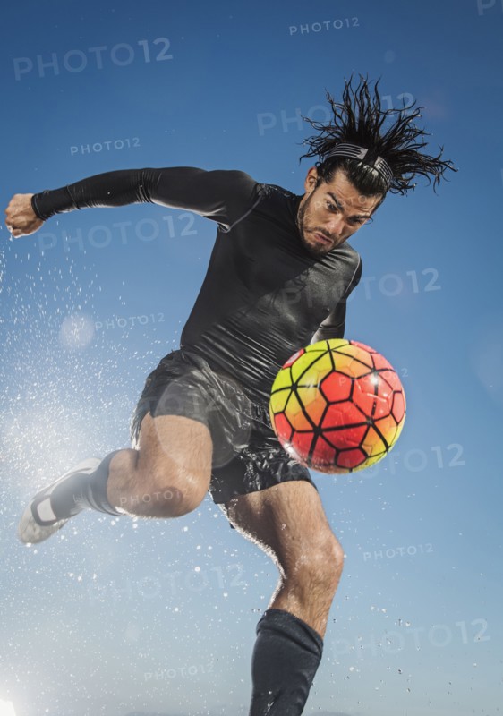 Water splashing on Hispanic man kicking soccer ball